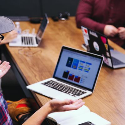 A photo of group of people around a table with laptops.  The person in the foreground has his hands upraised in a shrugging gesture, as if he is asking a question.